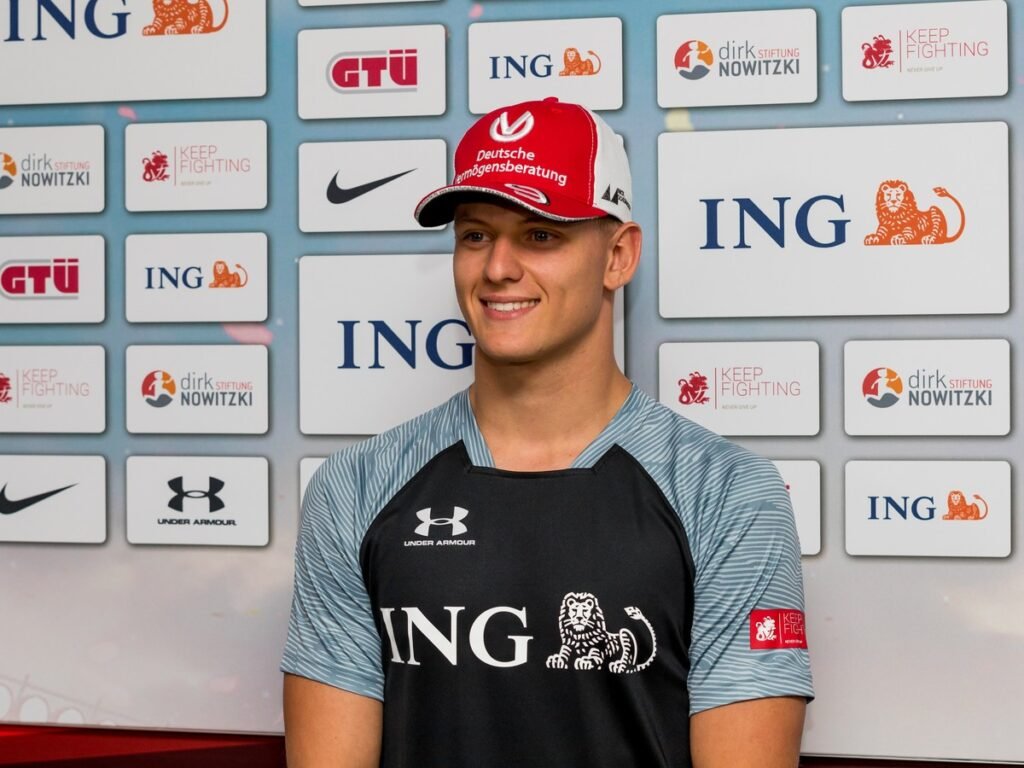 Mick Schumacher Freundin: Wer ist Clara Ramos? Mick Schumacher lächelnd vor einer Sponsorenwand beim Benefiz-Event ‚Champions for Charity‘ – seine neue Freundin ist Clara Ramos
